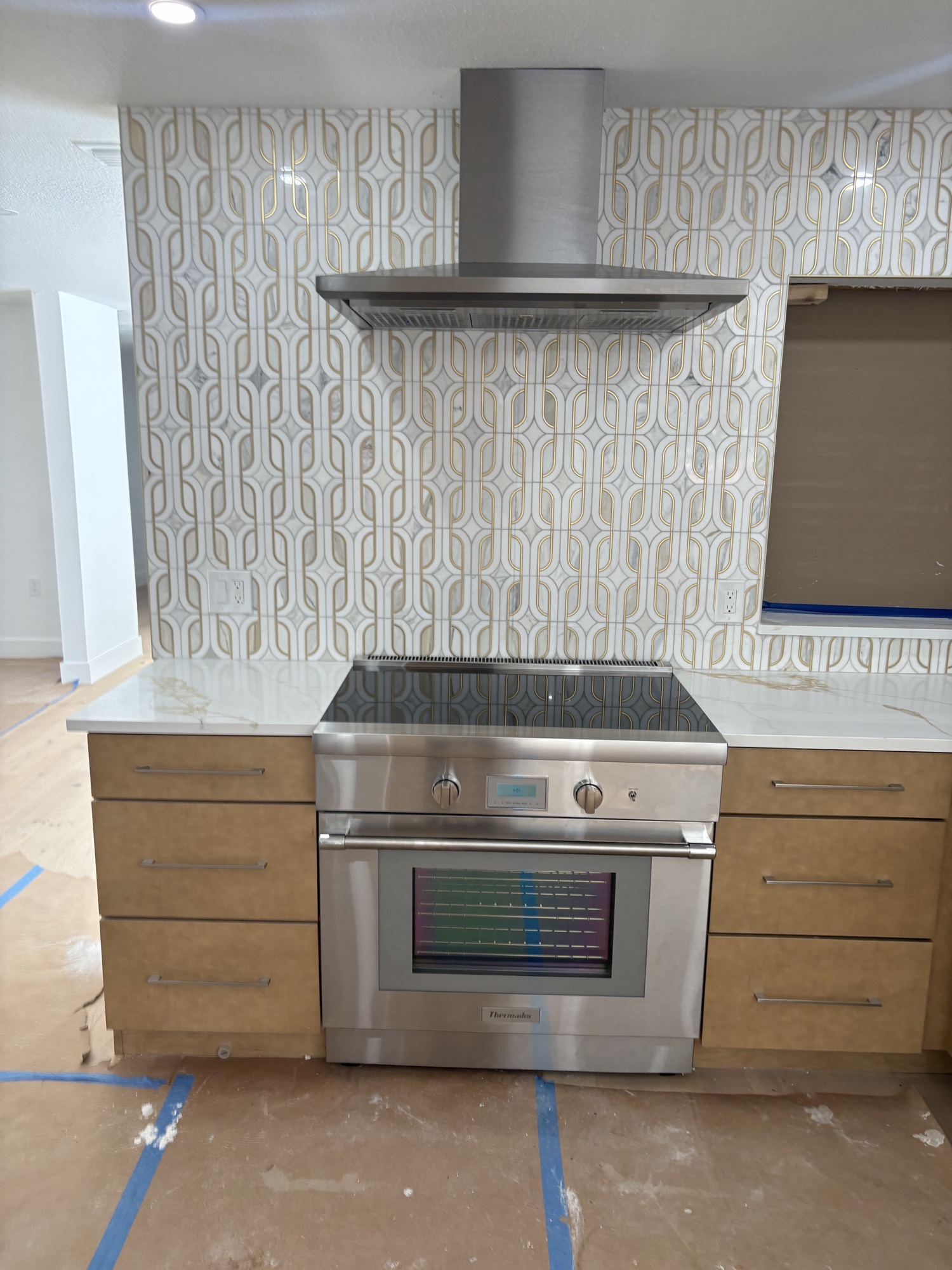 Thermador range and chimney hood installation with gold mosaic backsplash