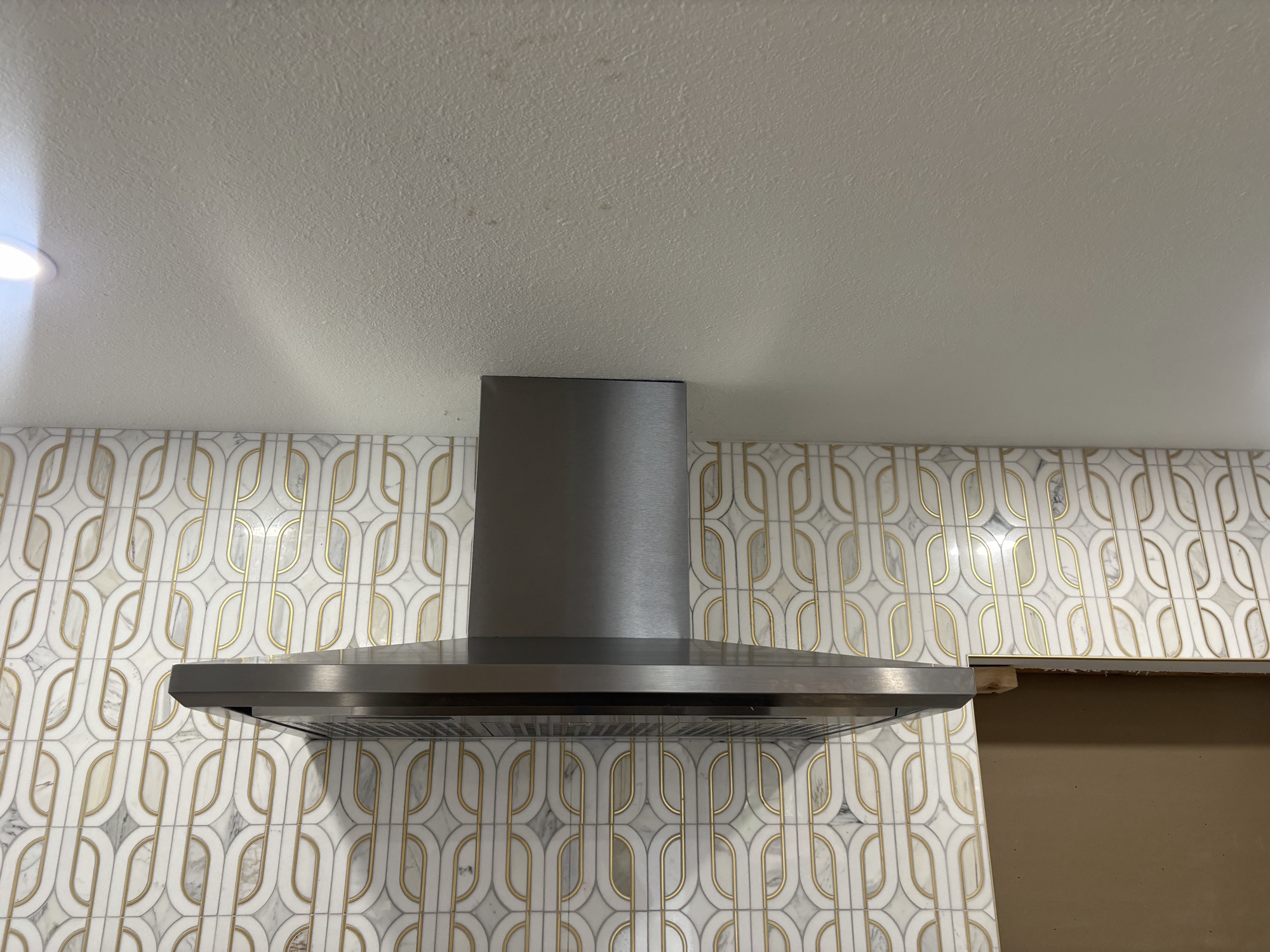 Chimney hood close-up against gold geometric tile backsplash