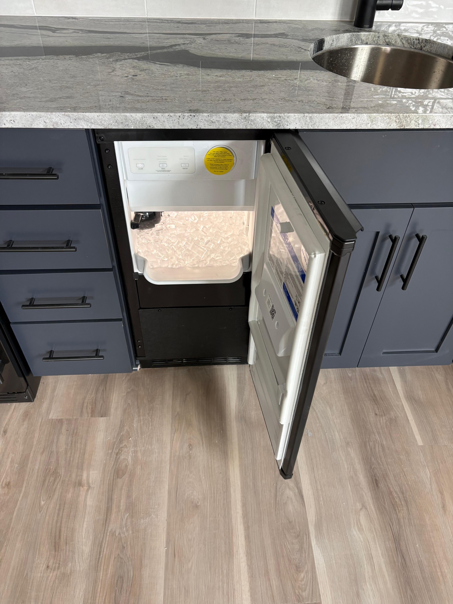 Under-counter ice maker installed in navy blue cabinetry with granite countertop